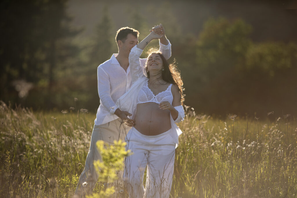 Shooting grossesse couple danse dans les champs, face à la forêt et le jura